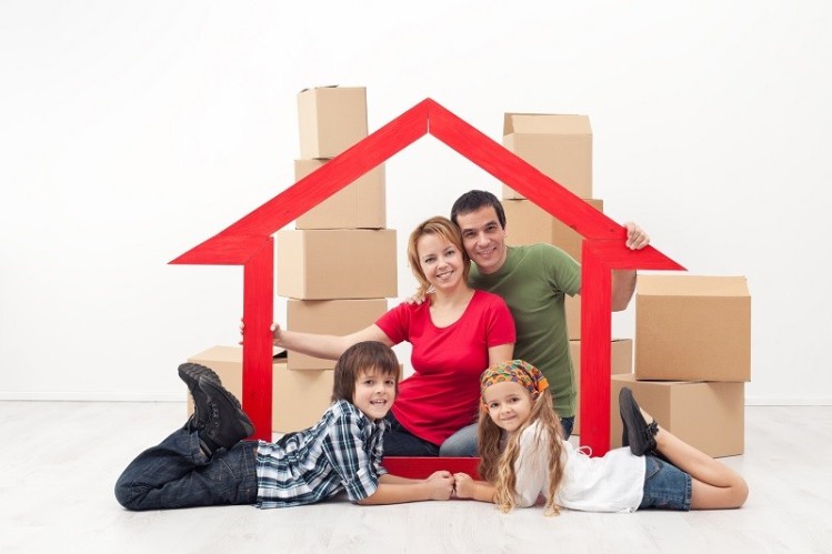 счастливая семья в макете дома на фоне картонных коробок